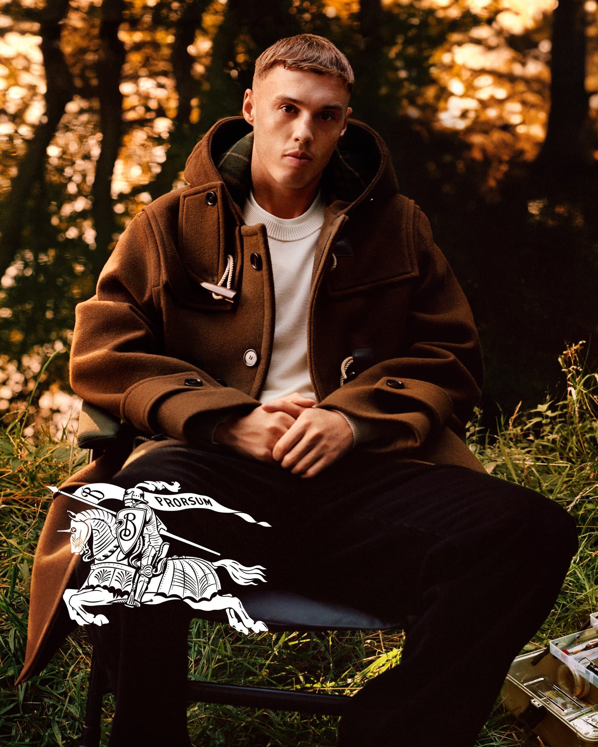 Cole Palmer sits beside a lake in a brown Burberry duffle coat